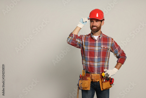 Professional builder in hard hat with tool belt on light background, space for text