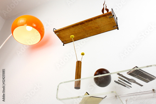 midcentury teak shelf on white wall in the living room with a wooden vase and a plack pen on it next to it a space age vintage orange lamp danish design front side low angle high view HIGH RESOLUTION photo