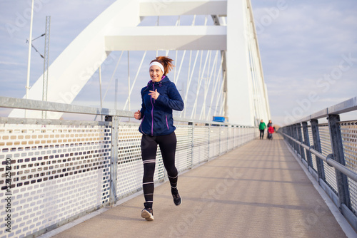 Young smiling woman running on the bridge footpath