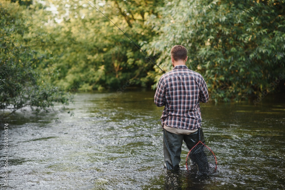 Man with fishing rod, fisherman men in river water outdoor. Catching trout fish in net. Summer fishing hobby Man with fishing rod, fisherman men in river water outdoor. Catching trout fish in net. Summer fishing hobby