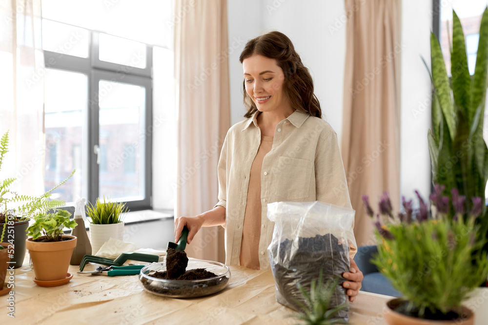 people, gardening and housework concept - happy woman with trowel and soil in bag planting flowers in glass vase at home people, gardening and housework concept - happy woman with trowel and soil in bag planting flowers in glass vase at home