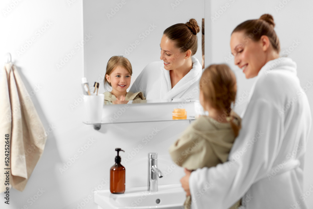 beauty, hygiene and people concept - happy smiling mother and daughter looking to mirror in bathroom beauty, hygiene and people concept - happy smiling mother and daughter looking to mirror in bathroom