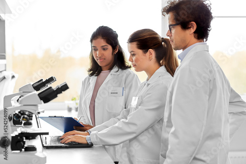 science research, work and people concept - international team of scientists with microscopes and laptop computer working in laboratory