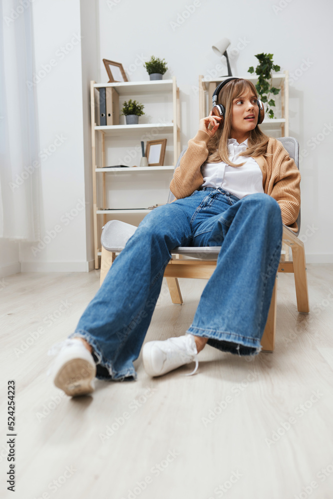 Dreaming happy young blonde lady in warm sweater in headphones looks aside listen fav songs sitting in armchair at modern home interior. Music time Relaxing Cool playlist Concept. Copy space Dreaming happy young blonde lady in warm sweater in headphones looks aside listen fav songs sitting in armchair at modern home interior. Music time Relaxing Cool playlist Concept. Copy space