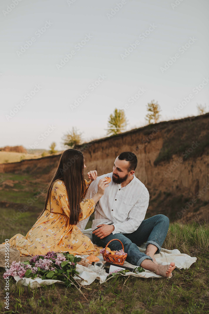 Couple in love have a picnic on a high hill. A girl feeds a croissant to her boyfriend at a picnic. 