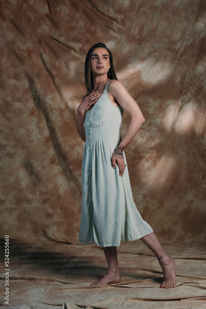 Full length of barefoot nonbinary person in dress standing on abstract background. Full length of barefoot nonbinary person in dress standing on abstract background.