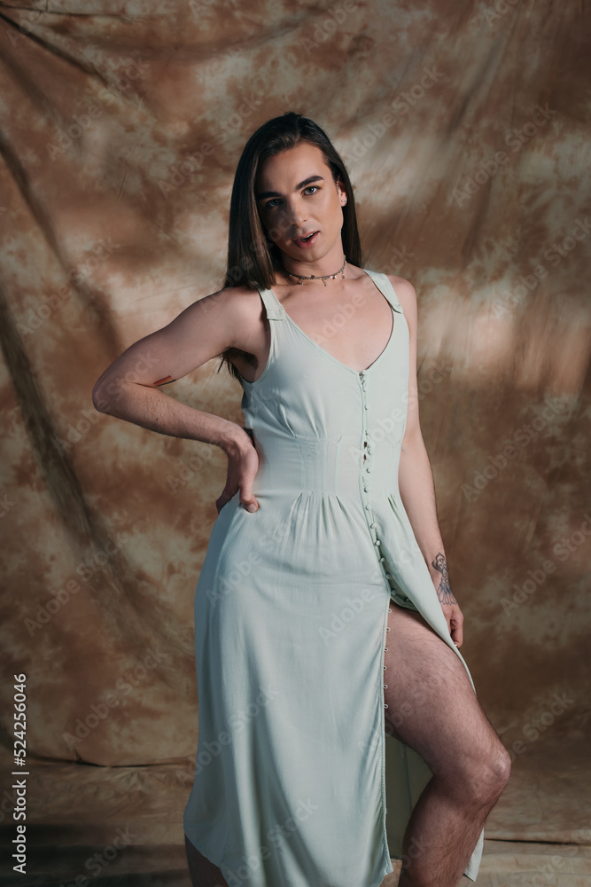 Fototapeta premium Brunette queer person in dress looking at camera on abstract background.