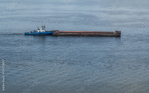 A small blue tugboat pushes a large barge down the river