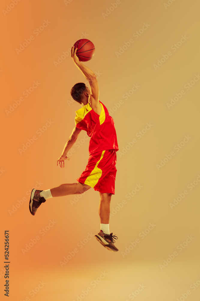 Portrait of young man, basketball player isolated over orange studio background in neon light. Scoring winning goal