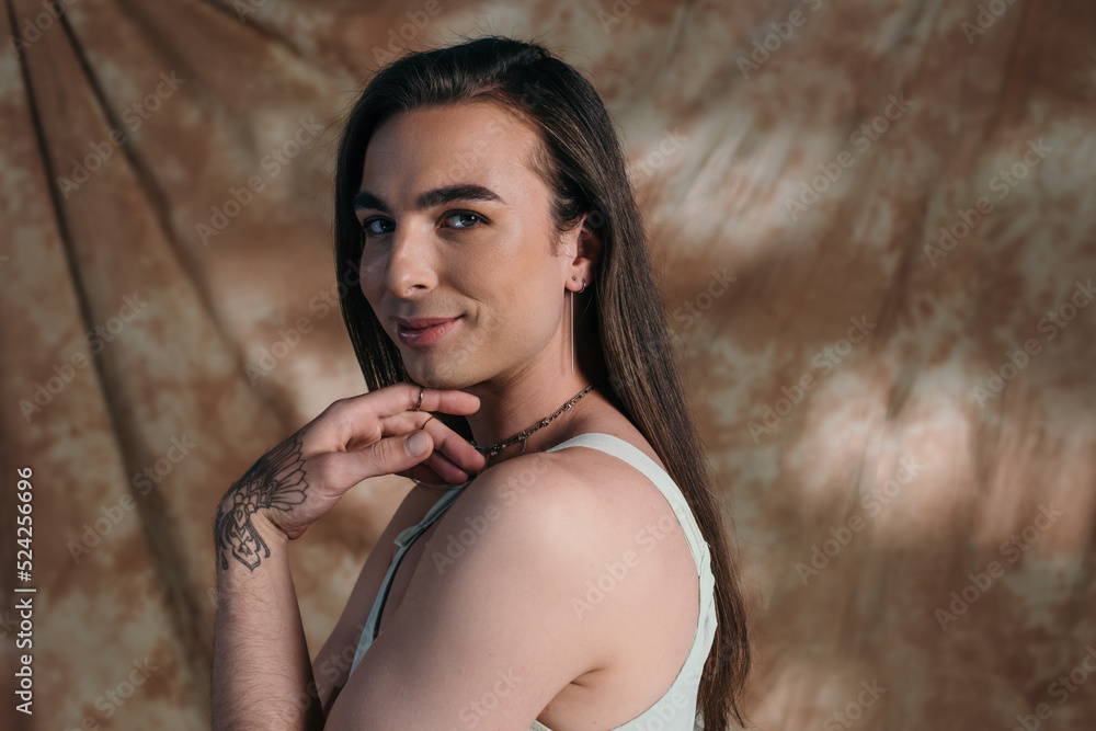 Smiling brunette queer person looking at camera on abstract background. Smiling brunette queer person looking at camera on abstract background.