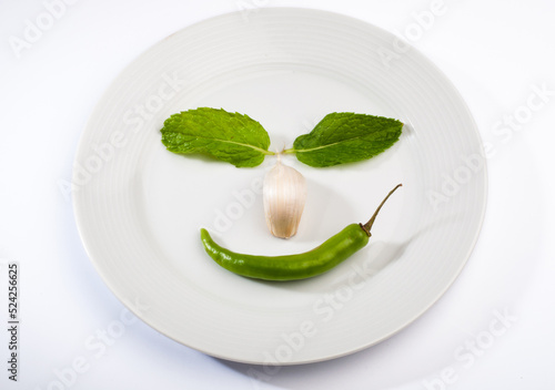 Funny face made with green herbs and spices on white plate. Fresh kitchen ingredients placed on a white plate.