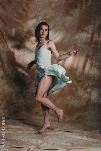 Positive queer person in sundress jumping and looking at camera on abstract brown background.