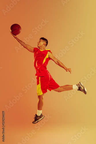 Portrait of young man, basketball player isolated over orange studio background in neon light. Match training © Lustre Art Group 