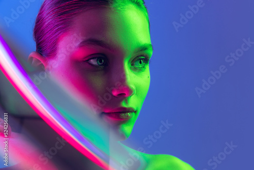 Portrait of young, beautiful and healthy girl with well-kept skin isolated on dark background in neon light. Art, fashion, style, facial expression
