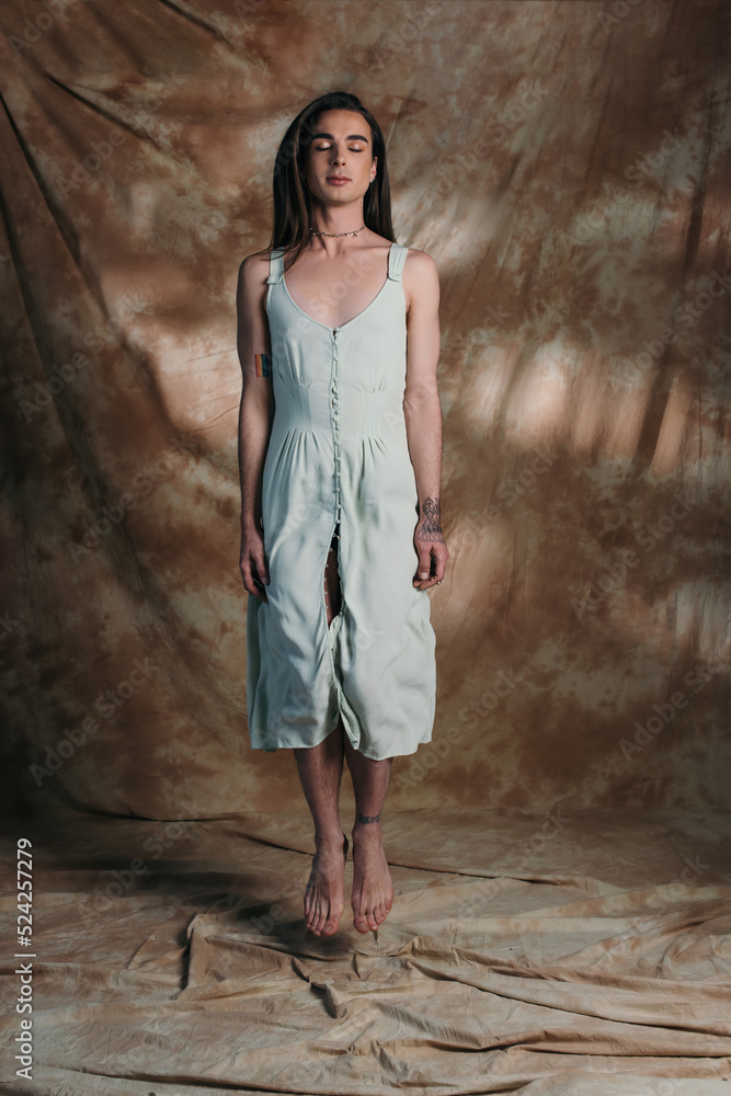Brunette nonbinary person in dress jumping on abstract brown background. Brunette nonbinary person in dress jumping on abstract brown background.