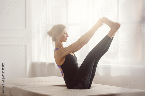 Athletic sporty blonde girl stretching in light yoga studio