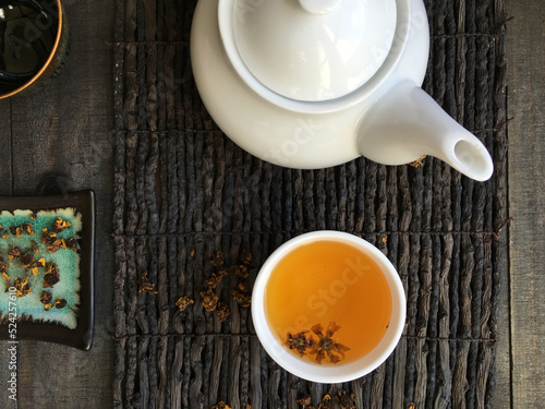 Bird eye view of a set up of an Asian tea ritual. White teapot and brewed herbal tea placed on a wooden mat.