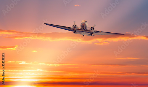 Vintage type old metallic propeller airplane in the sky, sunset clouds with calm sea in the background © muratart