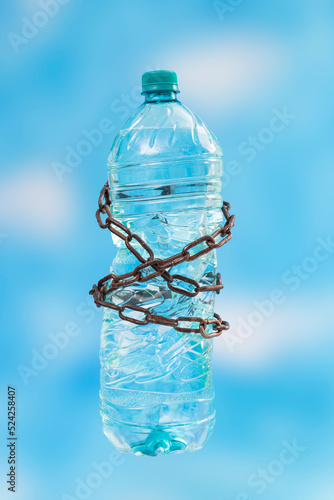 Plastic water bottle tied with rusty chains on blue skyes background. photo