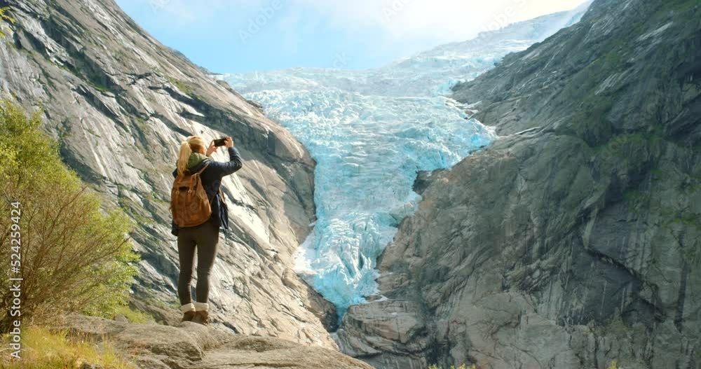 Global warming, melting glaciers and rising sea levels on rocky mountains view in nature. Back view of ecologist doing research outdoors. Woman looking at a landscape and taking photos with a phone Global warming, melting glaciers and rising sea levels on rocky mountains view in nature. Back view of ecologist doing research outdoors. Woman looking at a landscape and taking photos with a phone