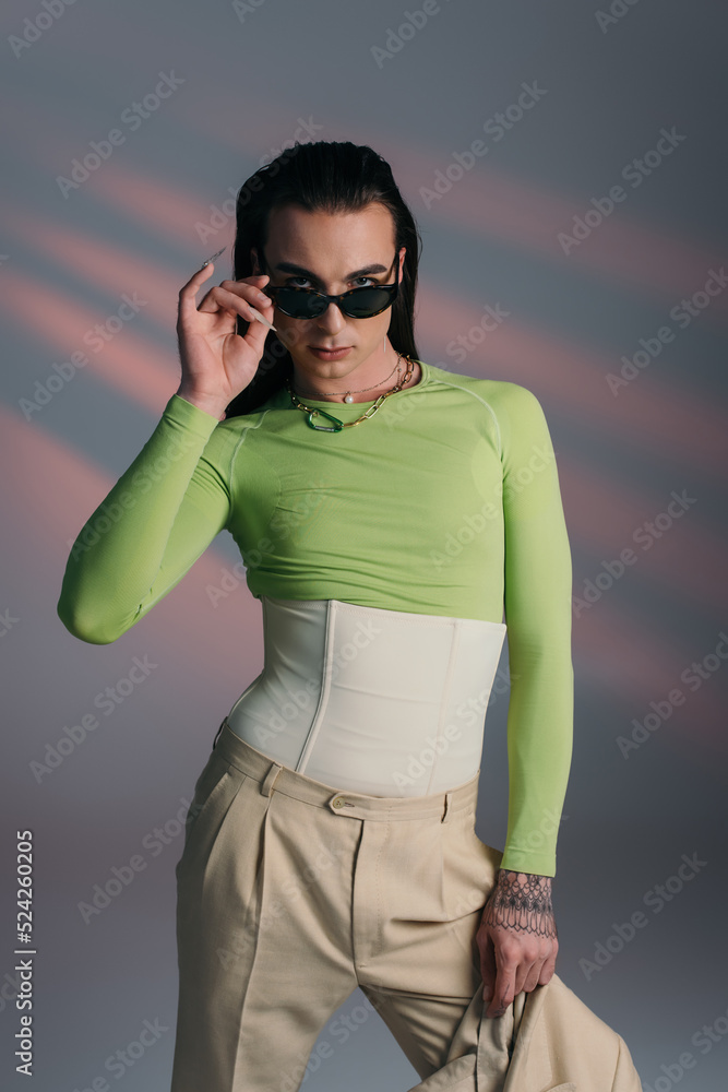Young queer model holding sunglasses and jacket on abstract background. Young queer model holding sunglasses and jacket on abstract background.
