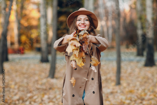 Young woman model in autumn park throws up yellow foliage maple leaves. Fall season fashion
