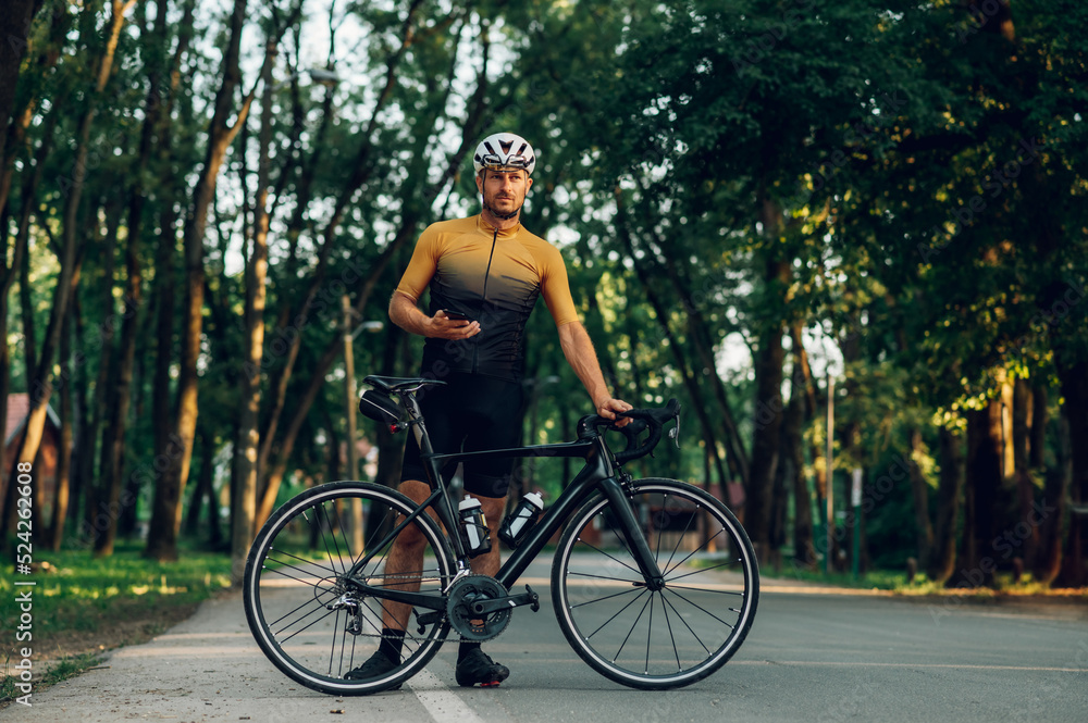 Athletic man in sport clothes riding a bike in the nature and using a smartphone