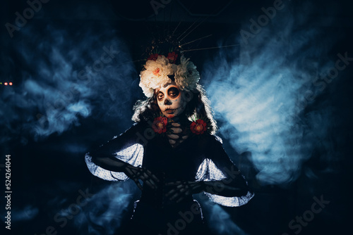 Woman with mexican skull halloween makeup in dark with backlight rays. Day of the dead aka Dia de los Muertos and halloween concept.