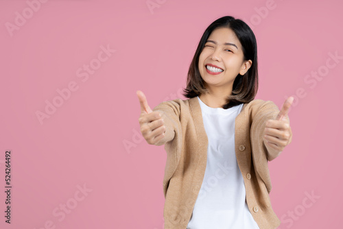 Foto Young smiling fun happy woman of asian showing thumb up like gesture blink isolated on pink background studio portrait