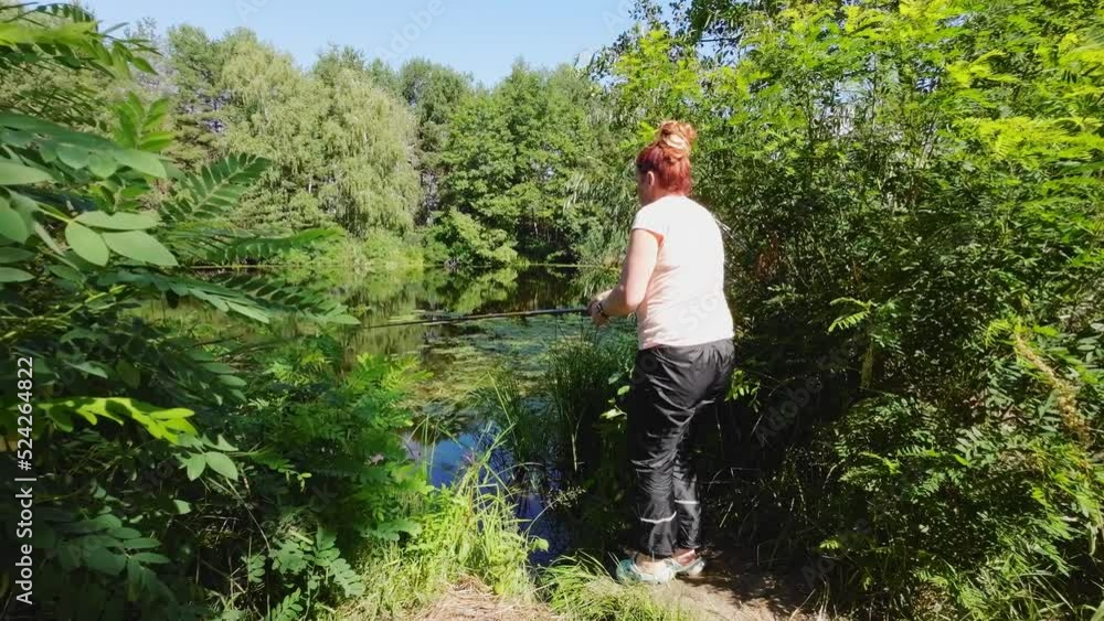 A woman is fishing on a fishing rod from the shore. A woman is fishing on a fishing rod from the shore.