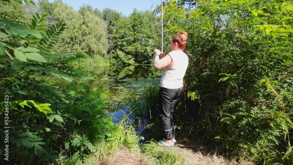 A woman is fishing on a fishing rod from the shore. A woman is fishing on a fishing rod from the shore.