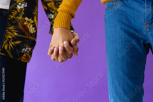 Mid section of biracial male couple holding hands on purple background