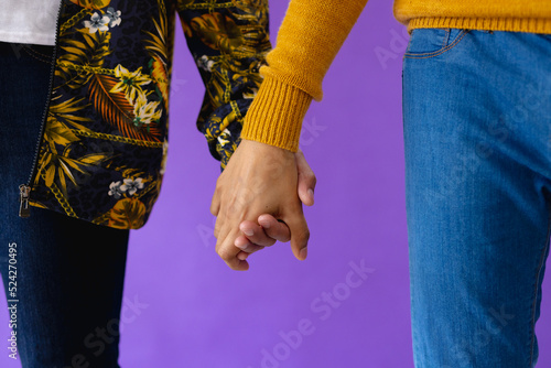 Mid section of biracial male couple holding hands on purple background