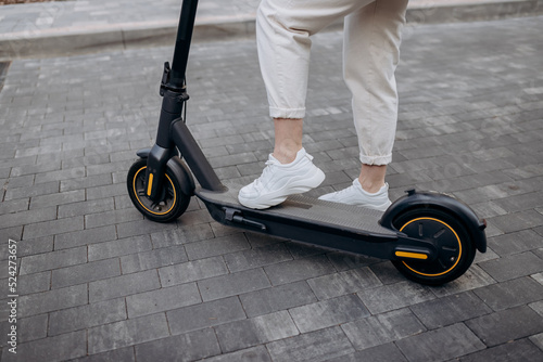 Close up of woman in white suit standing on her electric scooter in city