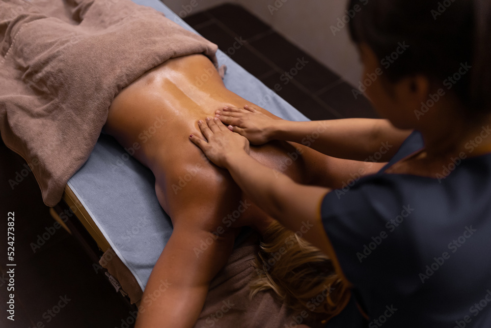 A masseur doing a hand and arm massage to adult woman in her back. Massage treatment in spa salon.