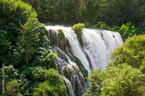 View of an incredibly beautiful waterfall among the dense greenery of trees  bushes and grass