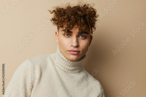  portrait of a handsome man, with curly hair, standing on a beige background in a light turtleneck, looking pleasantly into the camera. A photo with an empty space for inserting an advertising layout