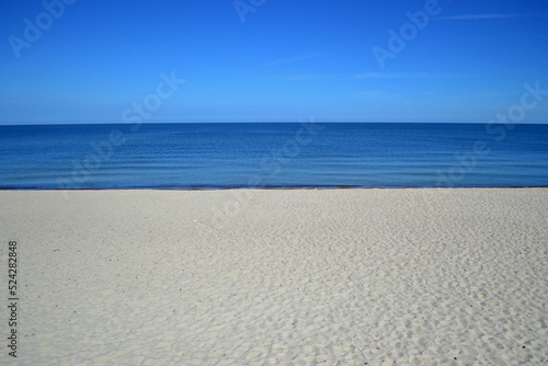 Beach on the Curonian Spit (Kurshskaya Kosa). Almost white sand. Blue calm Baltic Sea. In the photo at three standing only sand, sea, sky. Idyll. Symmetrical horizontal photo, Kaliningrad region