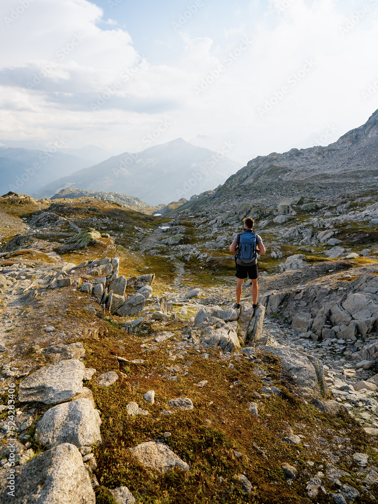Hiker at the top of the pass with a backpack to enjoy a sunny day in the Alps. Mountain lake nearly fusing with the surrounding granite boulders, sediment gray Grimselsee lake.