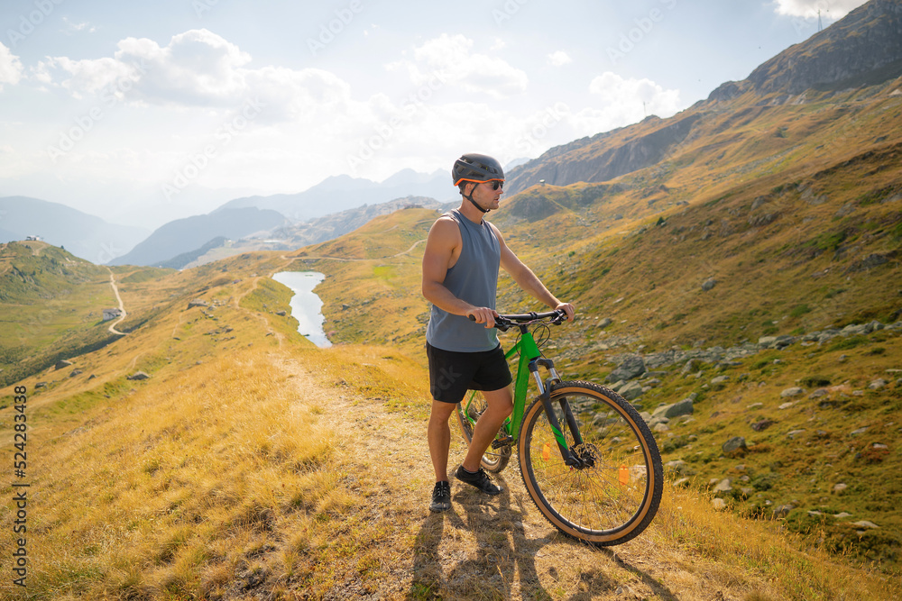 Male mountainbiker on a trail in the mountains. Young cyclist watching from the top of the mountain, enjoying the beautiful sunny day. Sports fitness motivation and inspiration.