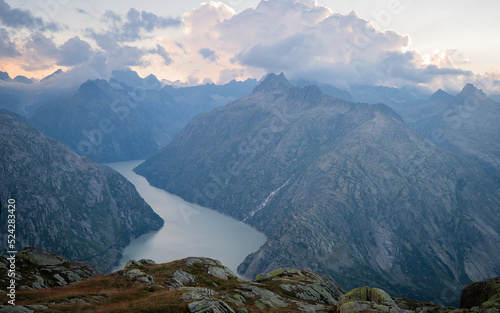 Panorama view of sediment gray Grimselsee lake in Switzerland. Amazing view on colorful clouds and layered mountains. Sunset or sunrise photo