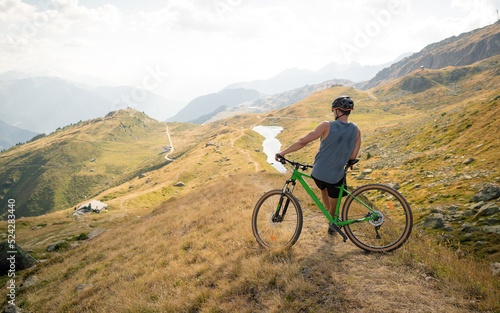 Fototapeta Naklejka Na Ścianę i Meble -  Male mountainbiker on a trail in the mountains. Young cyclist watching from the top of the mountain, enjoying the beautiful sunny day. Sports fitness motivation and inspiration.