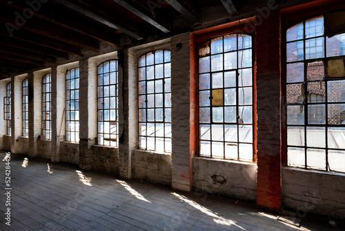 Windows of a ruined factory wall with old and broken mat glass and corroded iron frames in a brick wall in an industrial lost place in Germany. Sun flashing into former production hall or workshop.