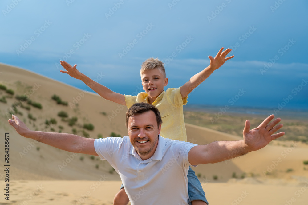 Father giving son piggyback ride outdoors at dune in mountains. Dad and teen boy walk together. Family travel, vacation, father's day concept. Father giving son piggyback ride outdoors at dune in mountains. Dad and teen boy walk together. Family travel, vacation, father's day concept.