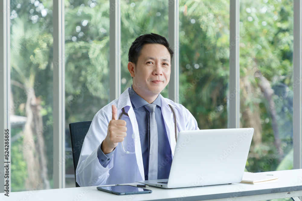 Portrait of asian senior doctor sitting in medical office while using laptop computer and posing thump up. Portrait of asian senior doctor sitting in medical office while using laptop computer and posing thump up.
