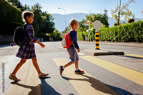 Foto Young pedestrians with backpacks walk to school and cross the road at crosswalk, back to school, school time, child safety, traffic road rules