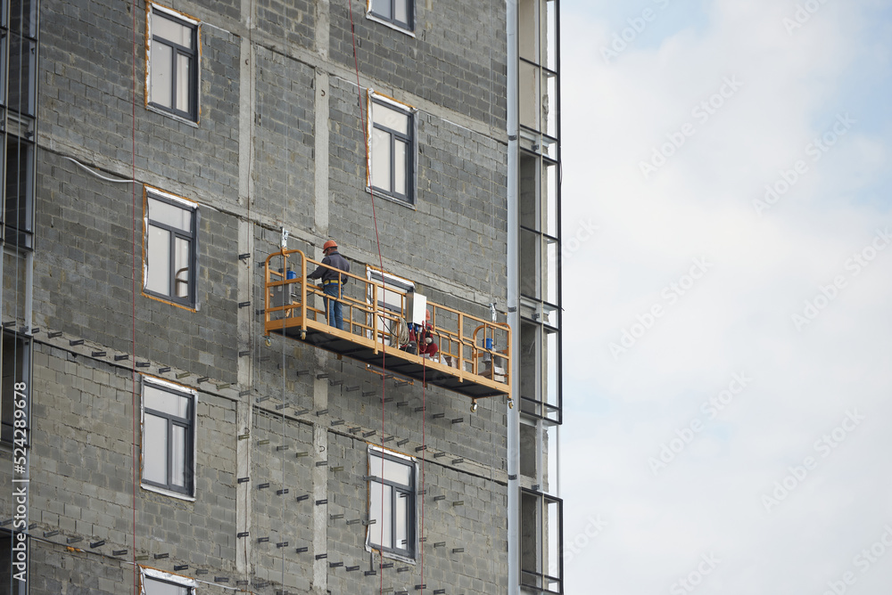 Builder works in a special suspended platform at the construction of an apartment building