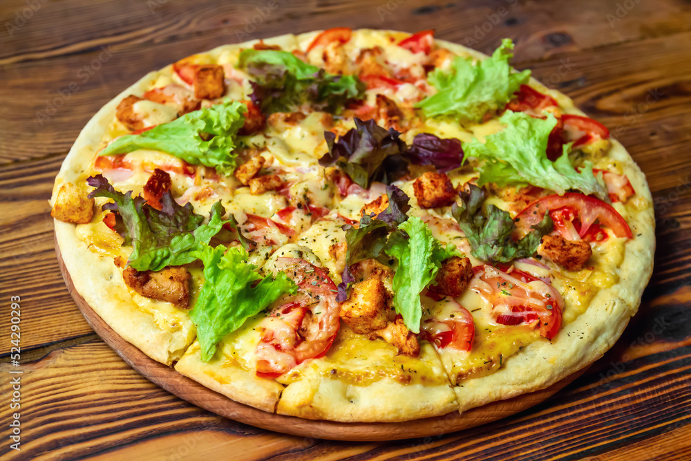 Pizza with chicken, cheese, tomatoes, lettuce and croutons on a wooden surface