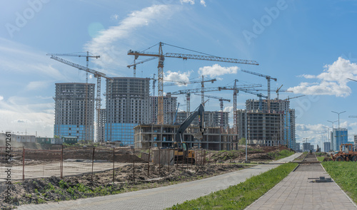 Construction of a multi-story residential buildings. Defocused foreground with young tree. Cranes work. Construction site.