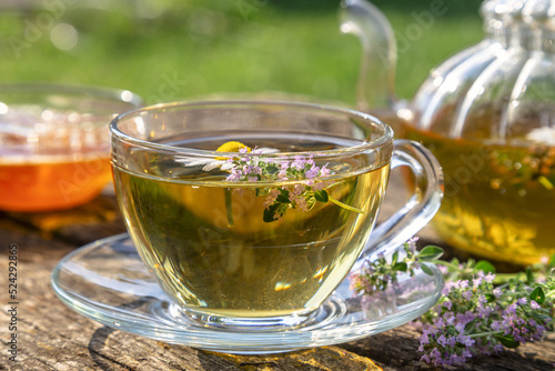 Herbal tea with chamomile and thyme in a transparent cup on an old wooden table on a sunny day